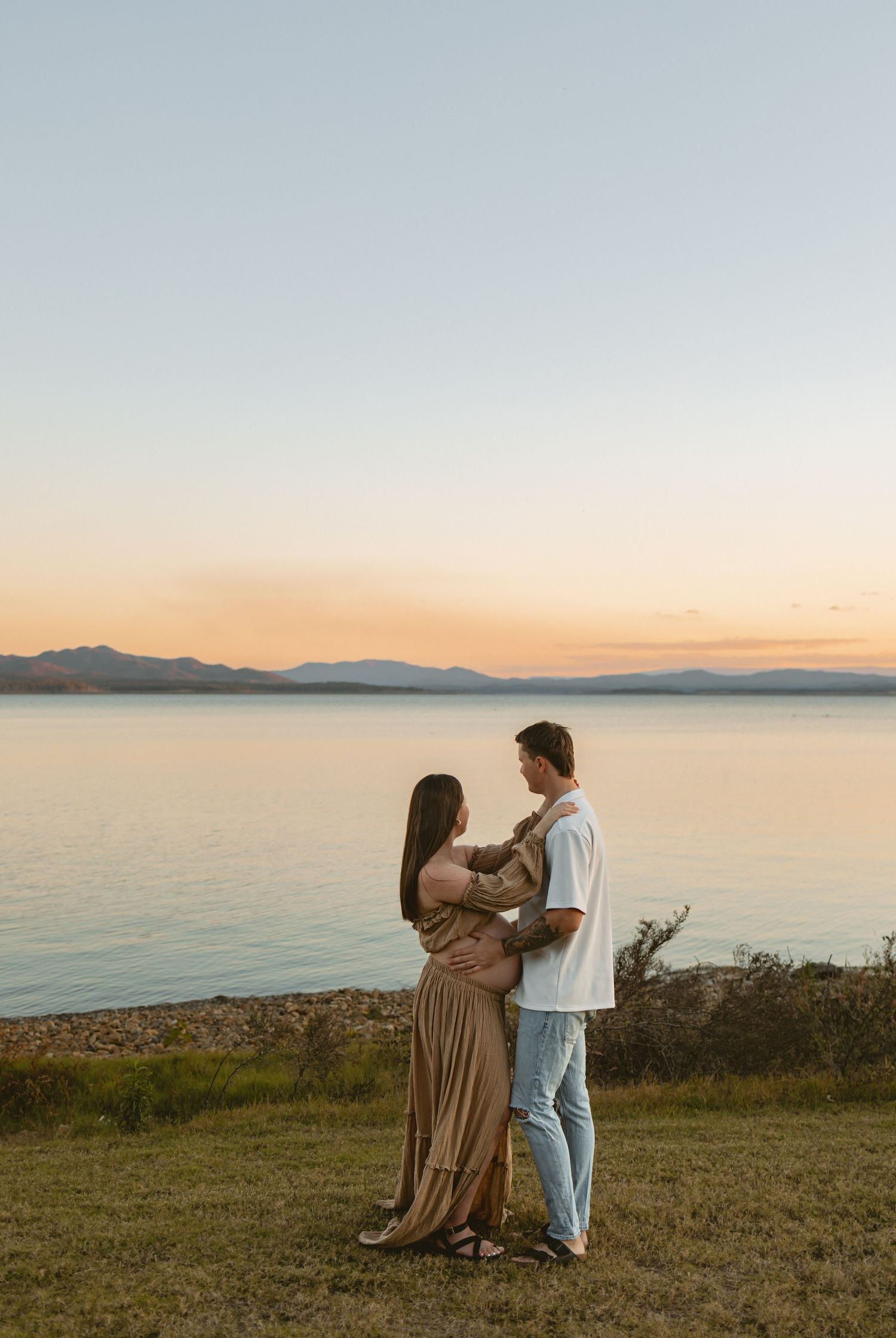 A couple shares an intimate moment against a sunset backdrop overlooking a serene ocean landscape.