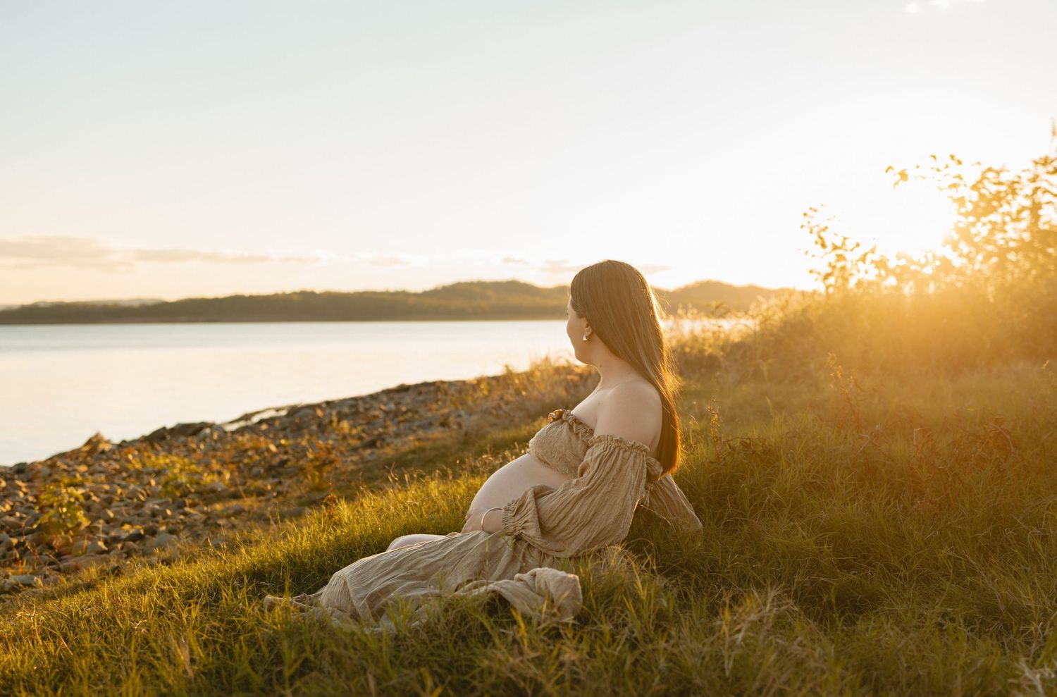A person sits on a hillside near the ocean at golden hour while the sun creates a warm glow across the scenic landscape.
