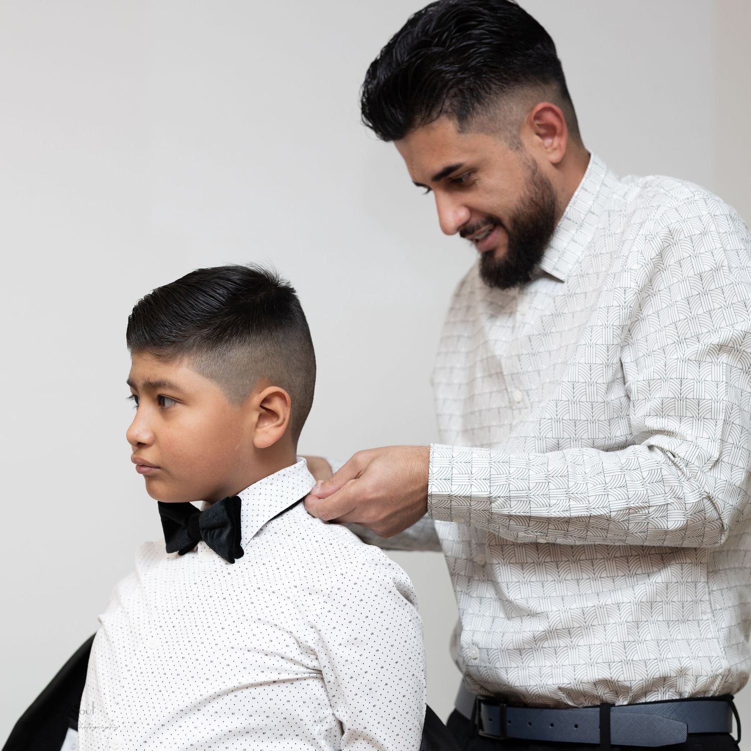 A heartwarming moment of bow tie adjustment during formal wear preparation.
