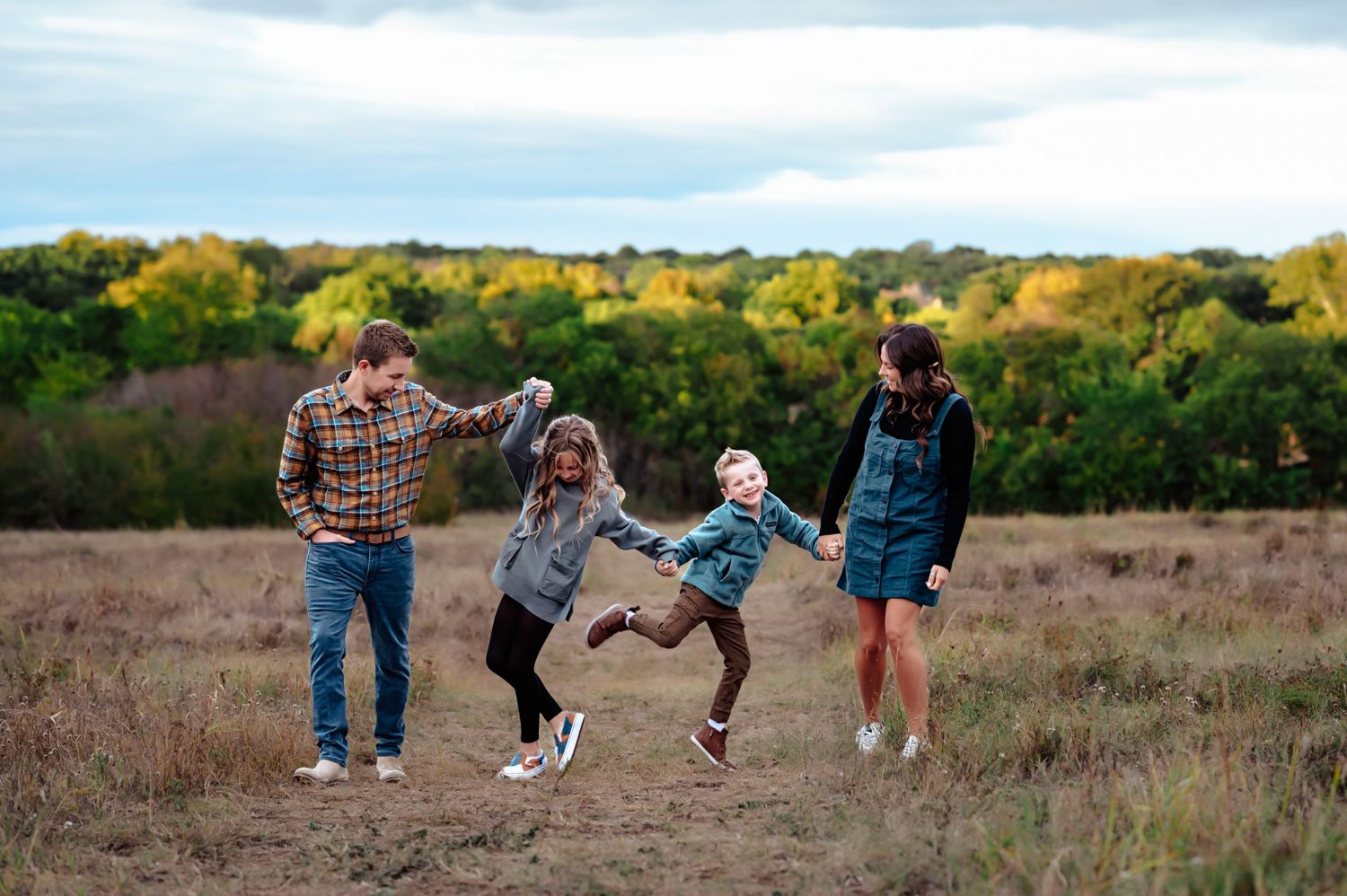 family of 4 holding hands dancing at nature preserve during fall family mini photo session by mesquite, tx family photographer