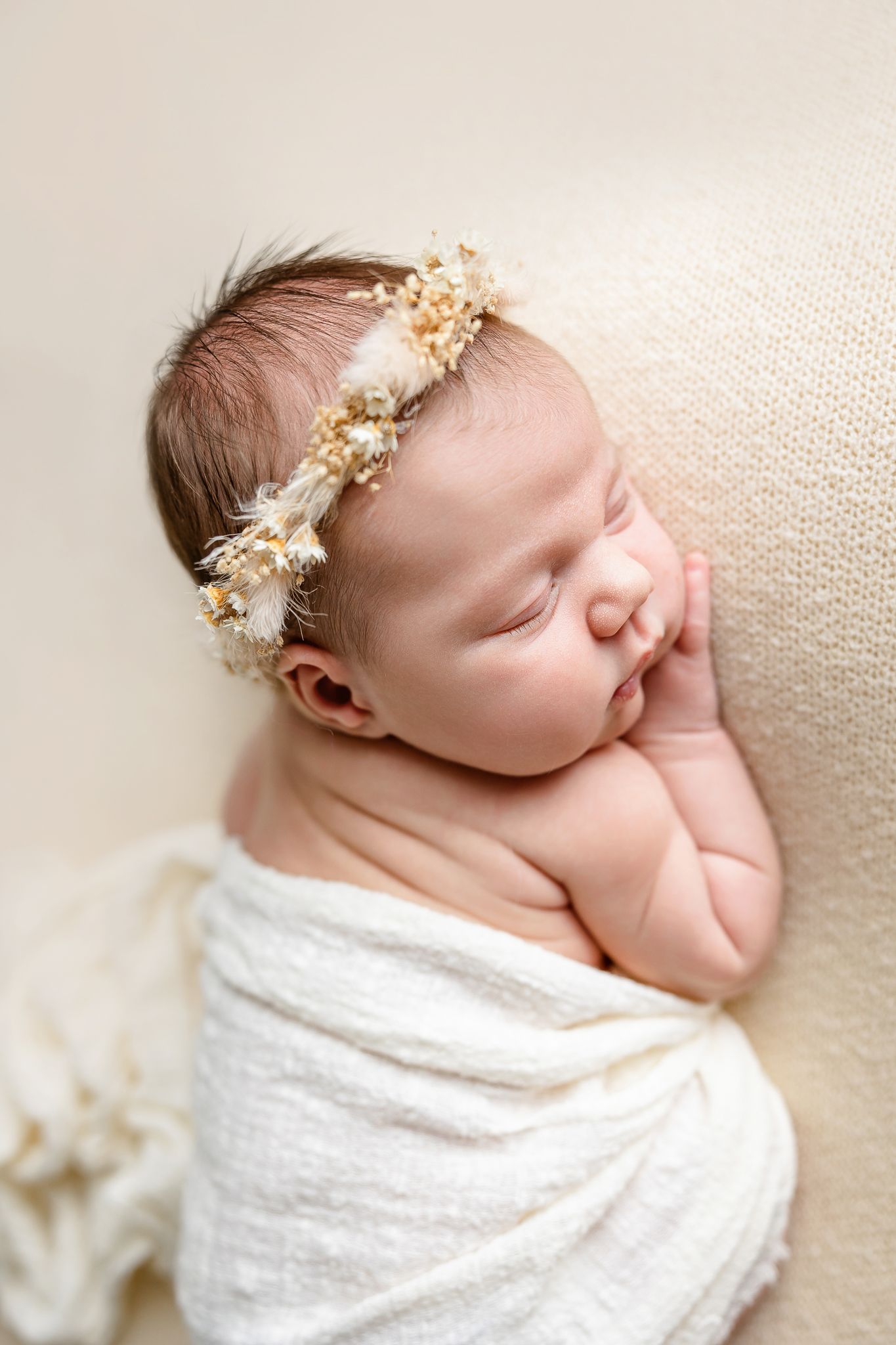 A peaceful sleeping newborn baby swaddled in soft gray knit fabric lying on a round white cushion.