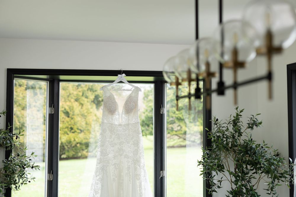 Elegant wedding ceremony setup with white chairs arranged in a sunny indoor greenhouse venue with large windows.