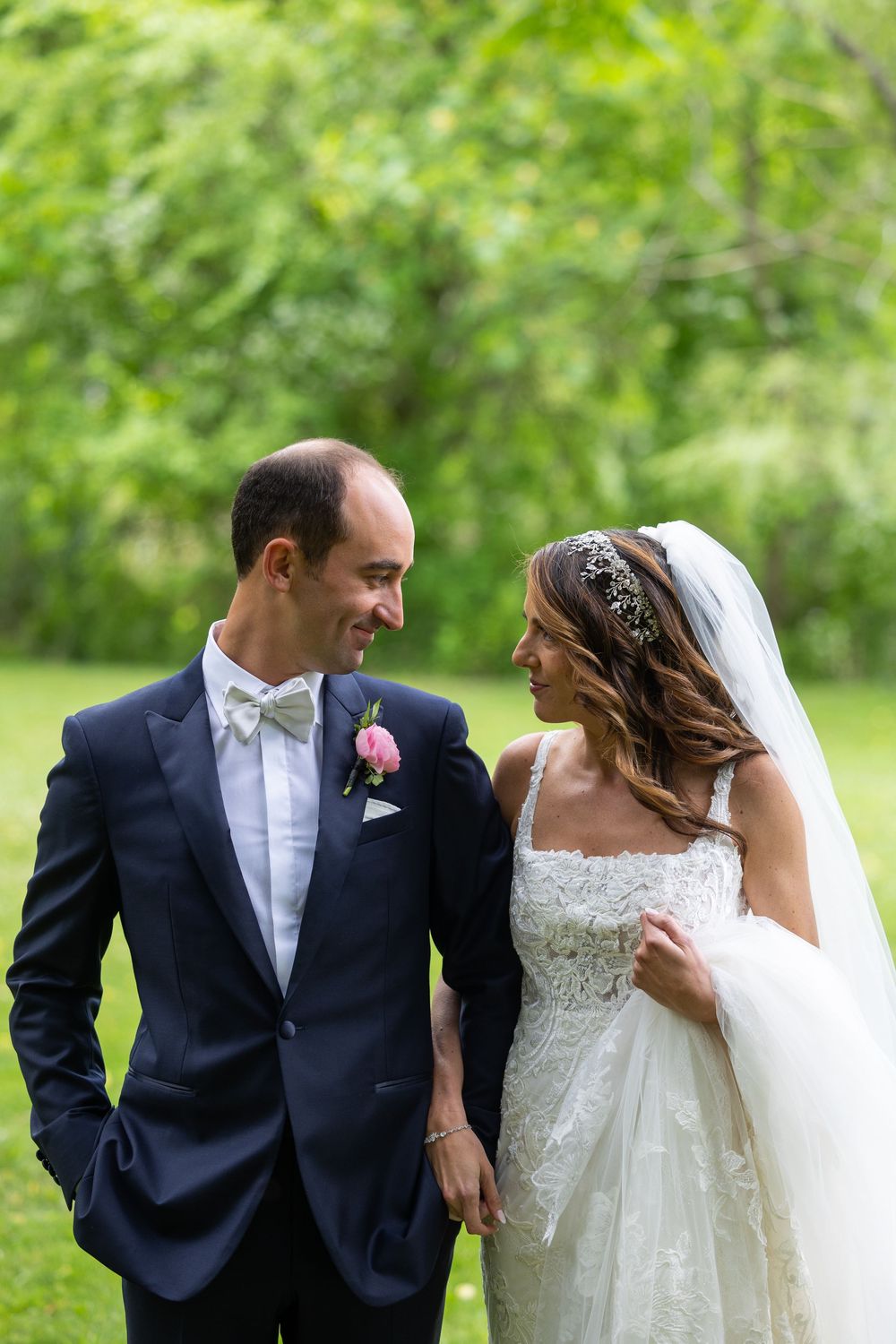 Newlyweds share a joyful moment together in a garden, with the bride in white lace and groom in navy suit.