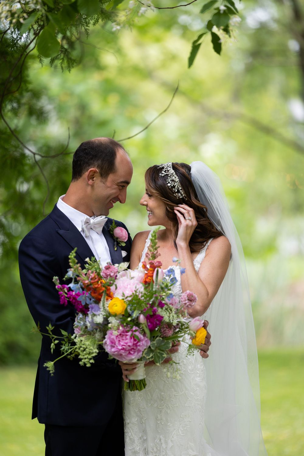 A bride and groom share a romantic moment outdoors with a vibrant multicolored wedding bouquet in a garden setting.