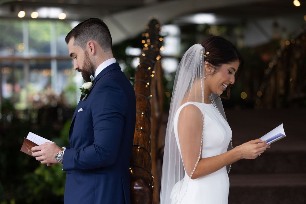 Bride and groom read letters back-to-back in a wedding venue illuminated by twinkle lights.