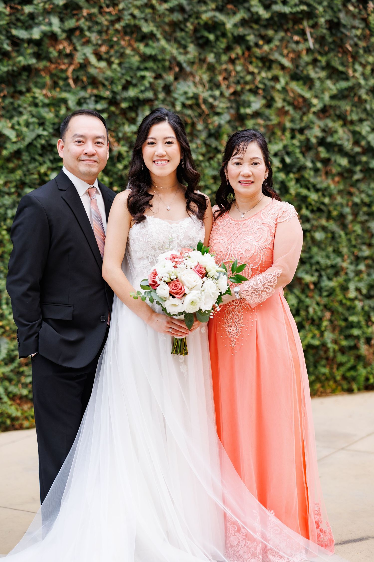 Bride posing with her parents for a group wedding photo outside
