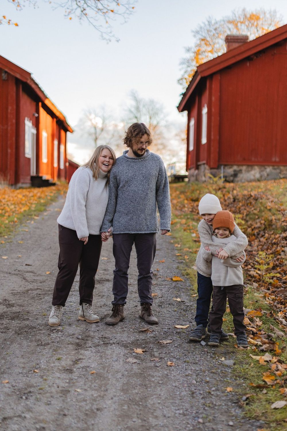 Family of four walking on a gravel path between red Swedish farm buildings during autumn.