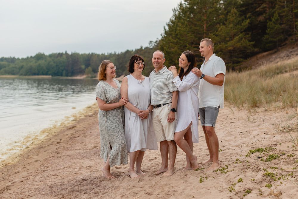 Happy family of five adults posing together on sandy beach with pine forest in background.