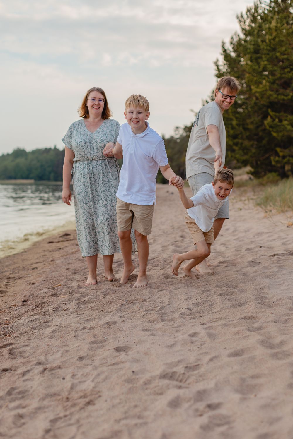 Happy family of four walking on sandy beach. Youngest boy playing tug war with dad. Perhekuvaus rannalla.