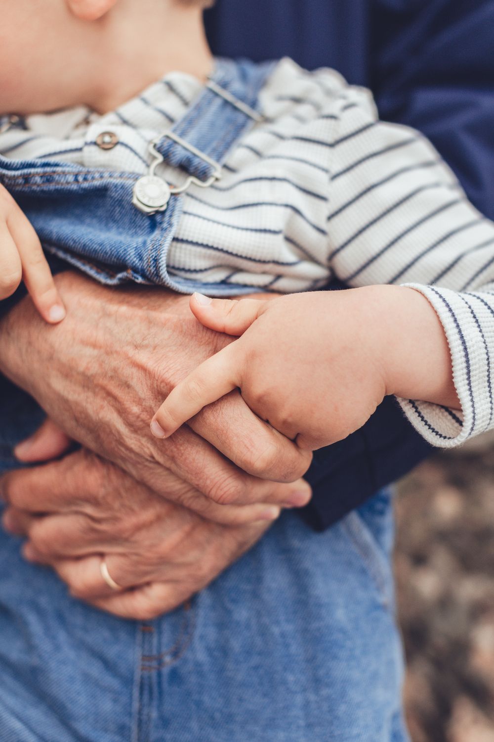 Close-up of elderly wrinkled hands holding a small toddlers hand while carrying child.