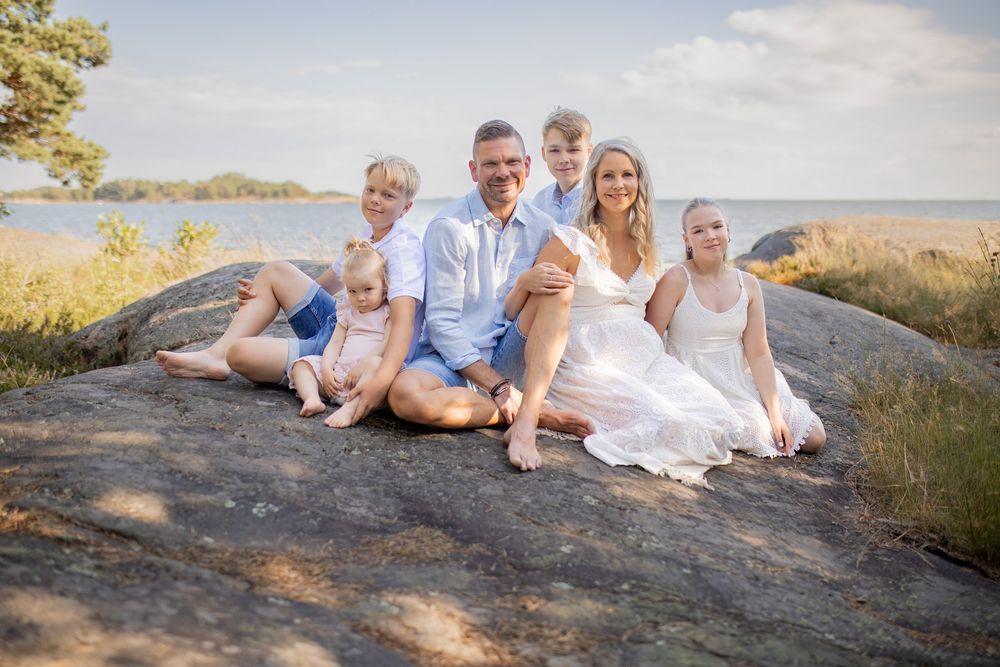 Perhekuvaus rantakallioilla. Suurperhe istuu viltillä katsoen kameraan. Valokuvaaja Annina Nygård, Uusimaa.