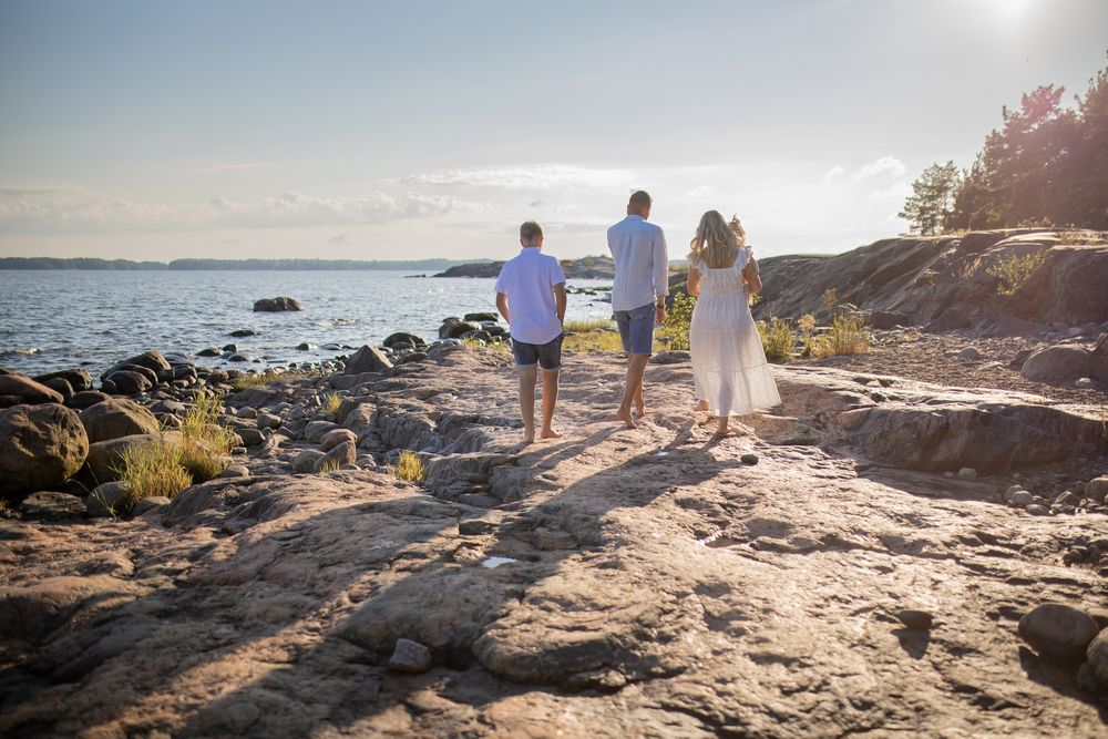Perhekuvaus rantakallioilla. Nelihenkinen perhe kävelee laakeilla kallioilla kohta auringonlaskua. Valokuvaaja Annina Nygård, Uusimaa.
