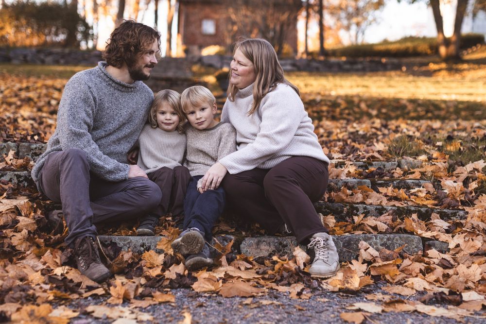 Family of four sitting on stone steps covered in autumn leaves, sharing a warm moment outdoors.