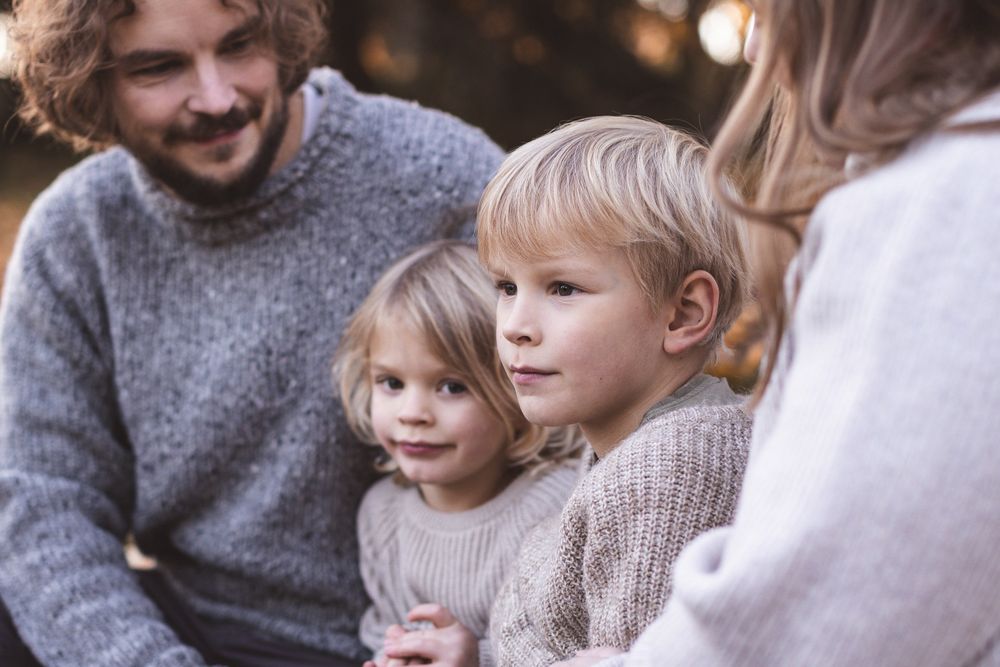 A young family with two blonde children sharing a warm moment outdoors in soft autumn light.
