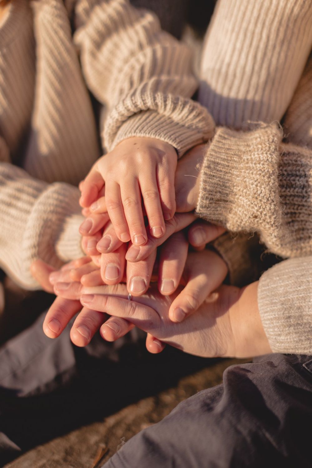 Multiple hands stacked together in unity, wearing cozy knit sweaters in warm neutral tones, symbolizing teamwork and togetherness.