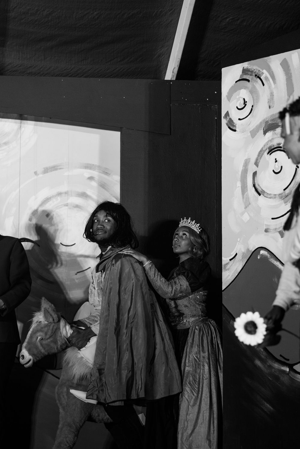 Performers in dark robes move across a dimly lit stage with white spiral patterns on the wall.
