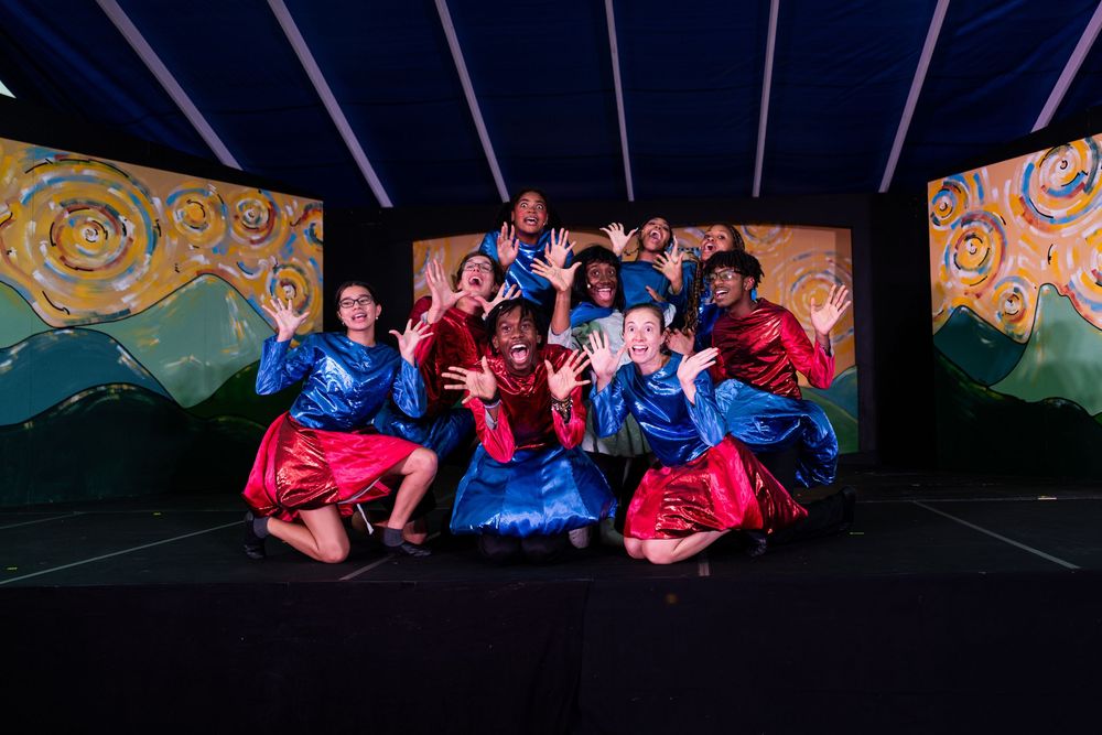 Performers arranged across a stage with colorful costumes and theatrical lighting.