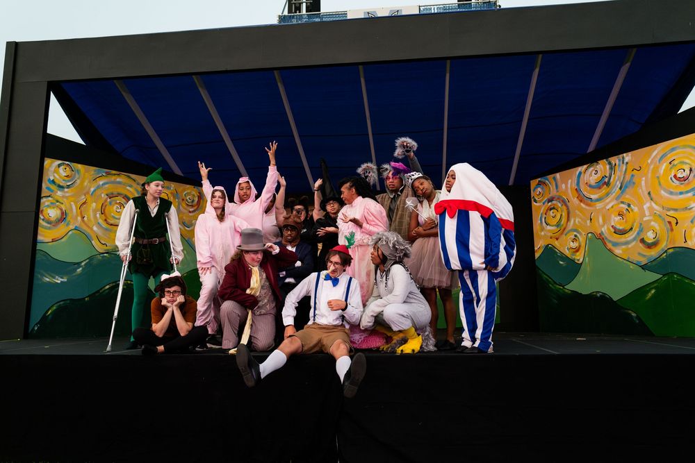 Theater performers on stage with colorful backdrop and lighting during a live performance.