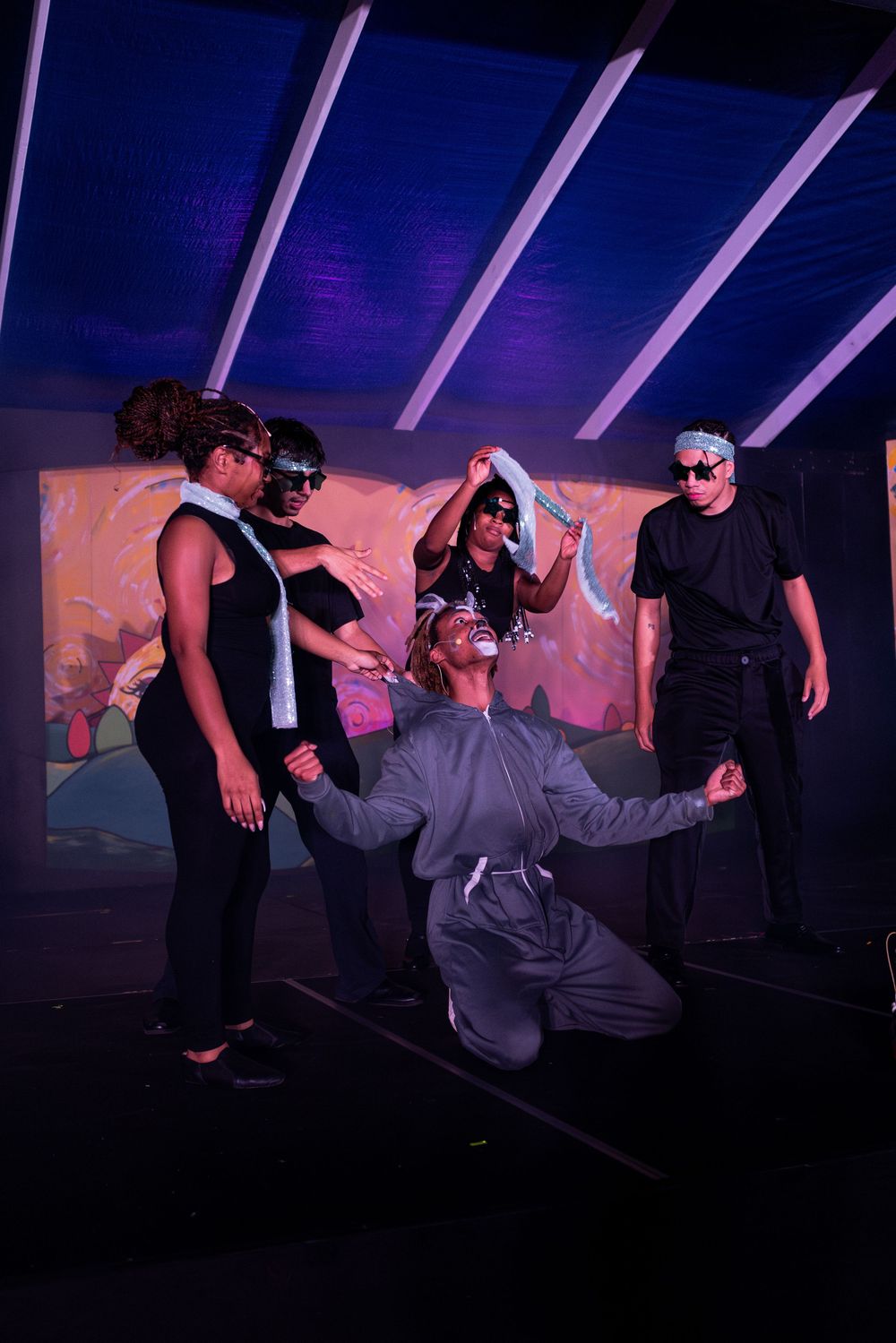 Performers creating dynamic movements on stage under purple theatrical lighting.