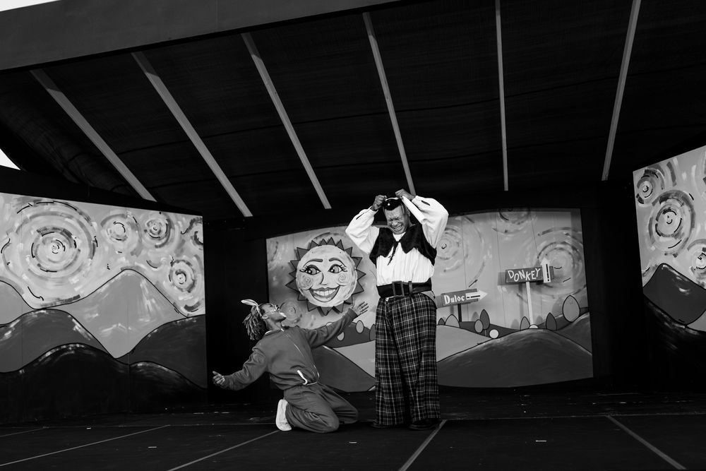Dark silhouettes of performers against a painted stage backdrop in monochrome.