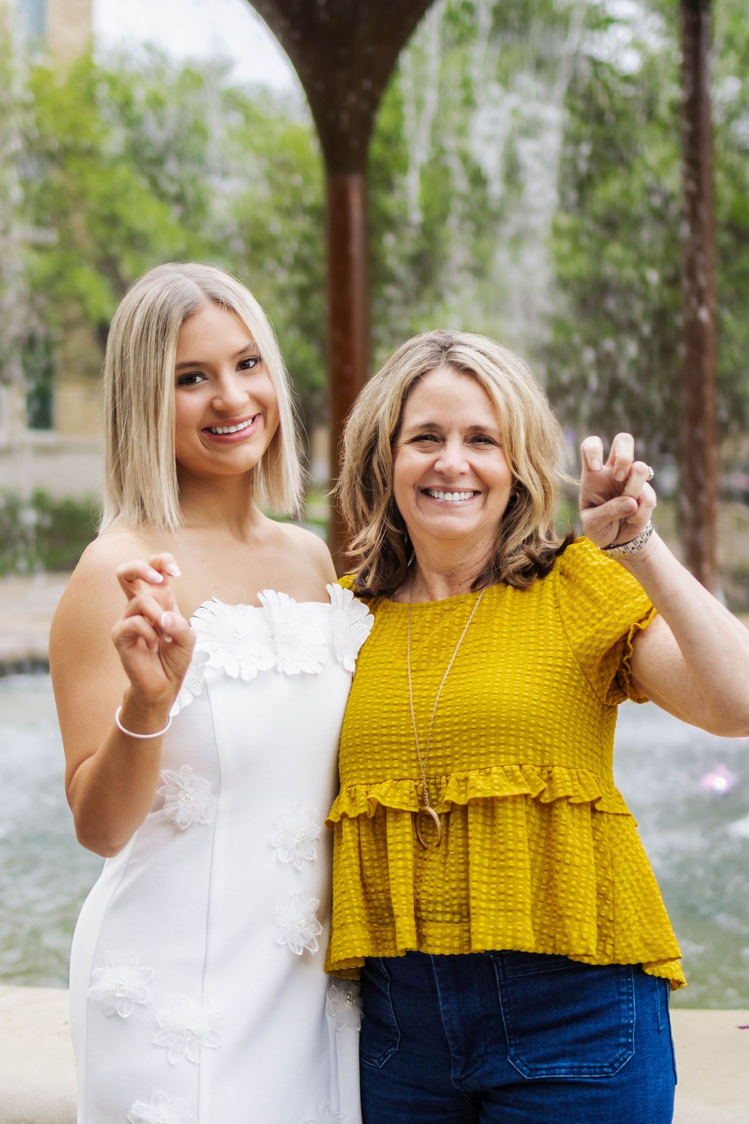 Two friends in white and yellow tops posing together outdoors with trees in the background.