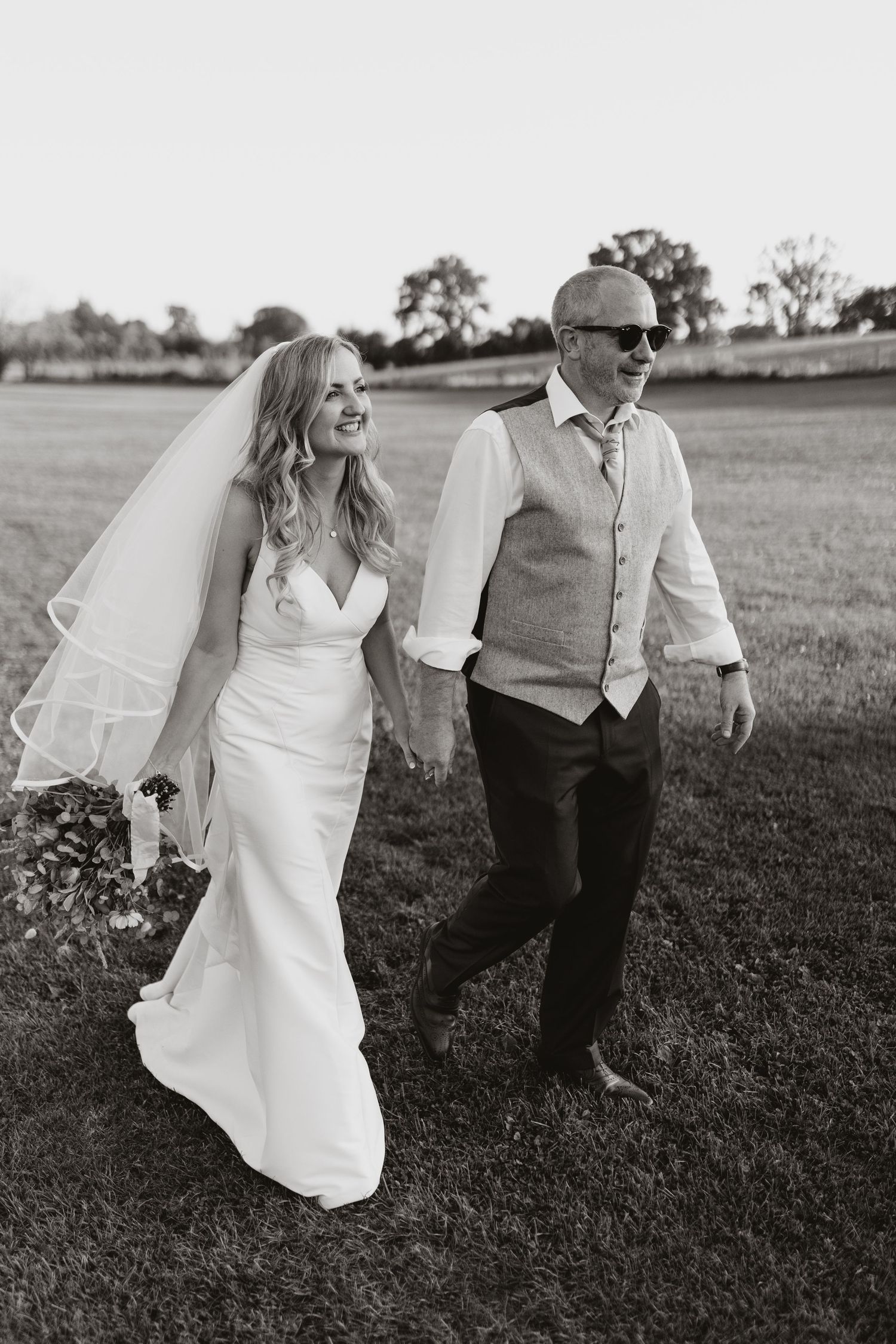 A joyful wedding couple dances together in a grassy field on a sunny day, captured in a sequence of black and white photos.
