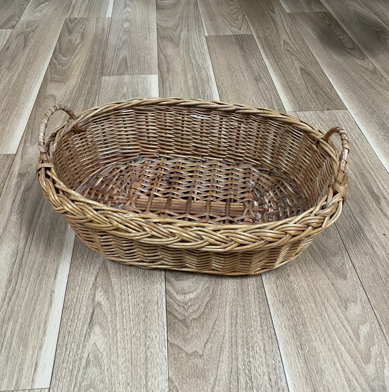Large woven wicker basket with handles displayed on wooden flooring.