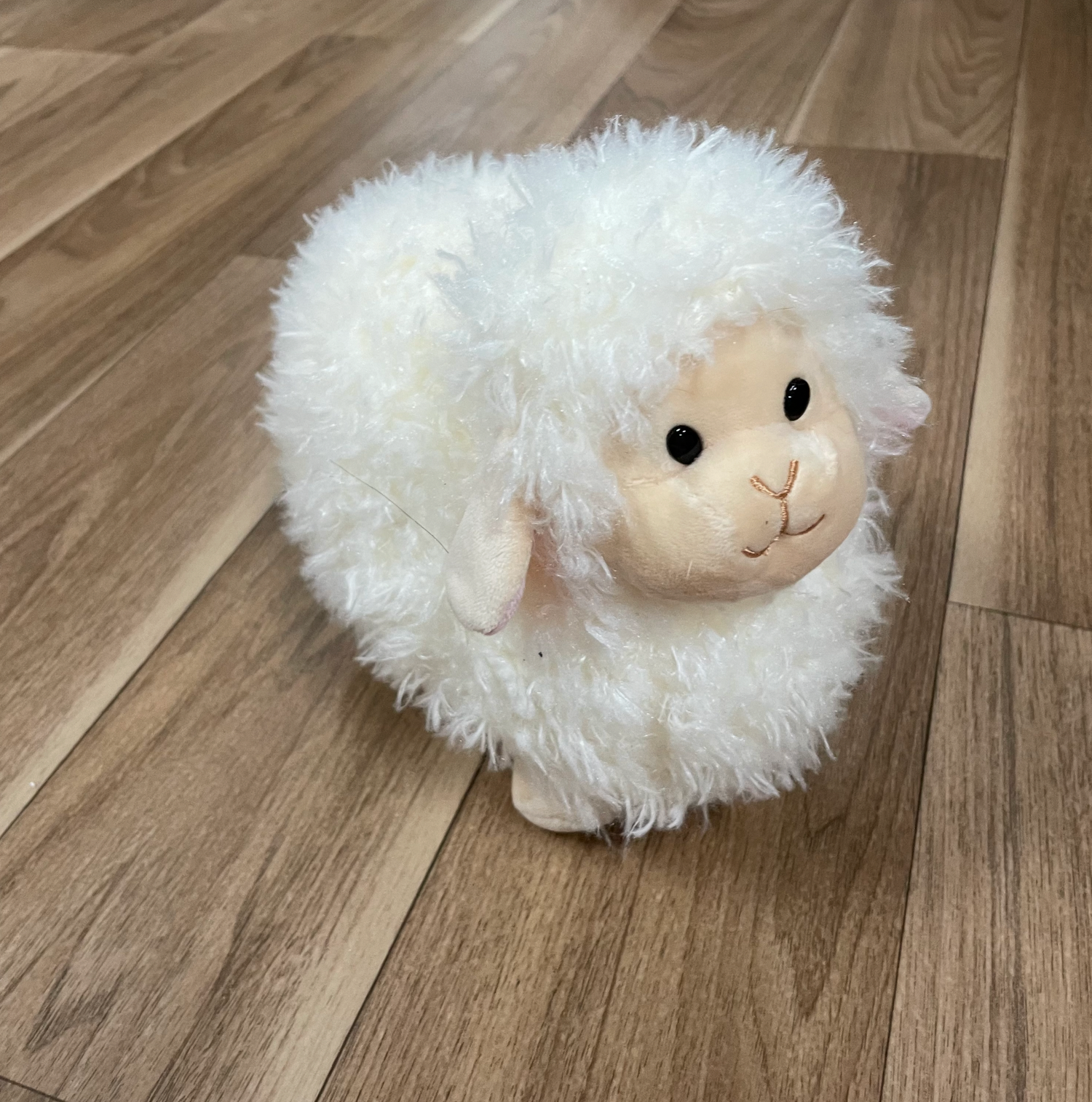 Fluffy white sheep plush toys displayed on wooden flooring.