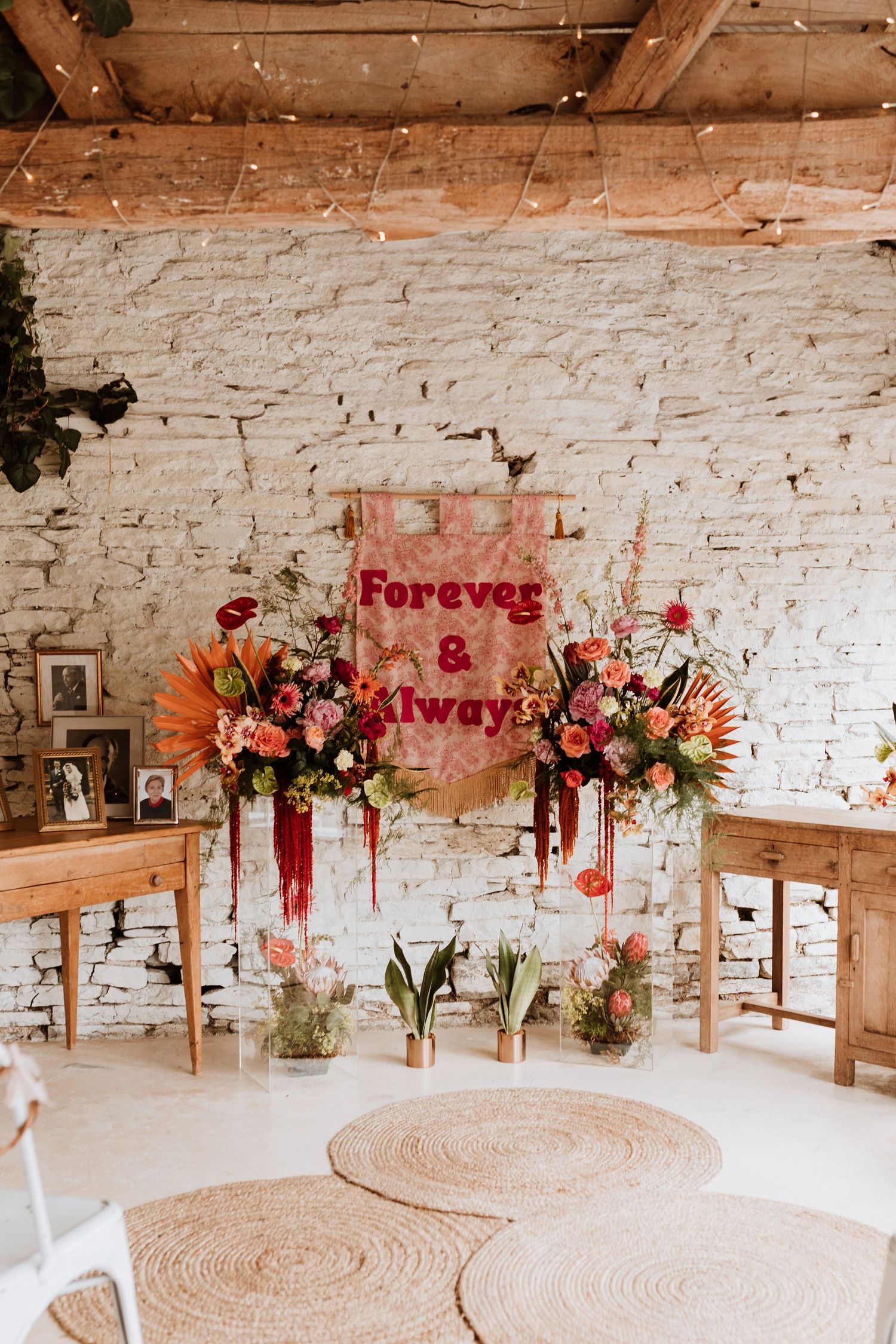 Rustic wedding decor with pink neon sign reading 'Forever & Always' against white brick wall with floral arrangements.