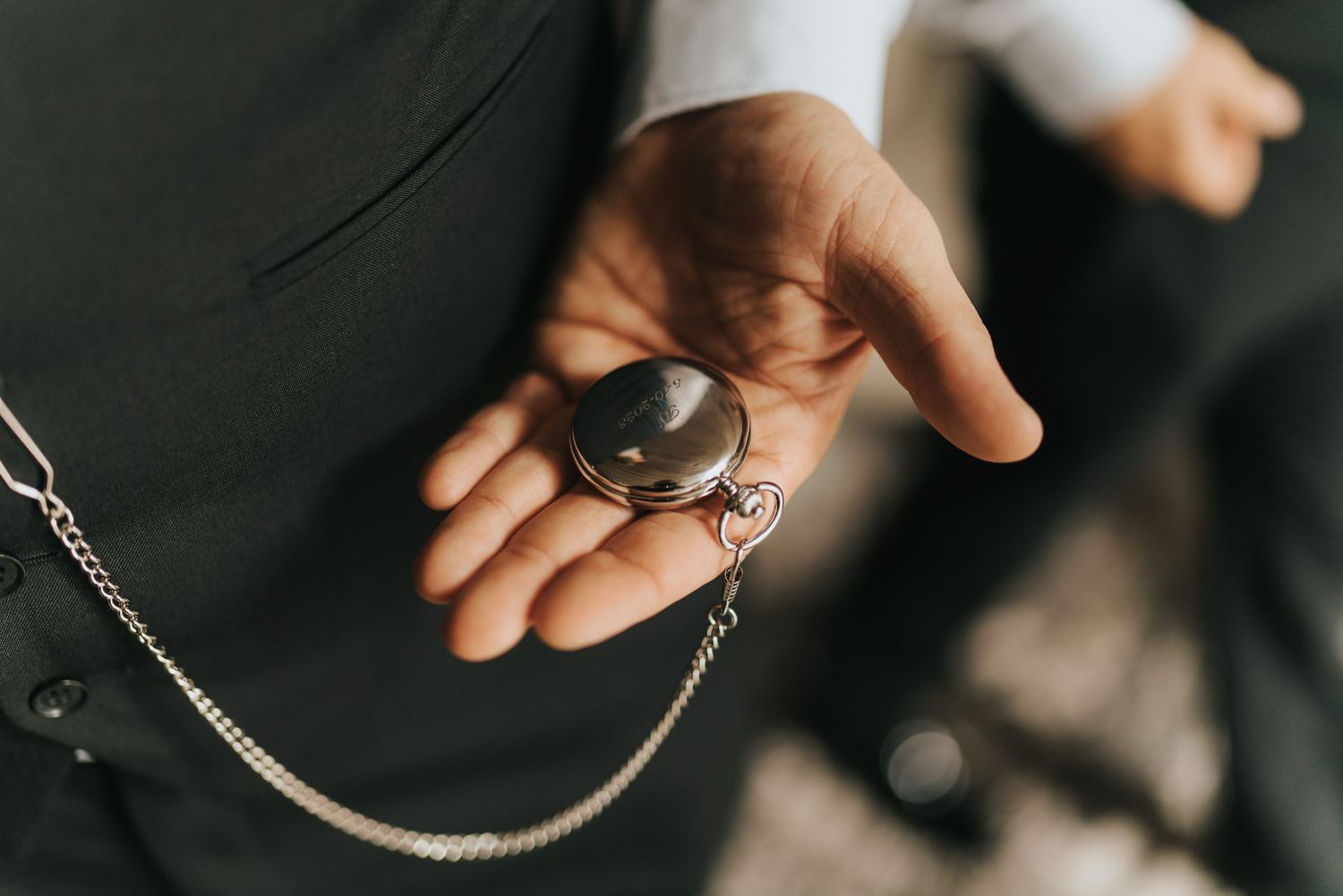 A hand holds a vintage pocket watch with a silver chain against a dark background.