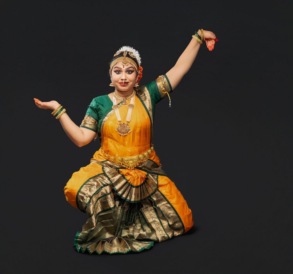 Classical Indian dancer in yellow and green costume performs expressive poses against dark background.