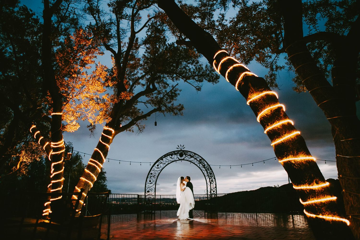 Trees wrapped in glowing spiral lights illuminate a moody evening wedding at Padua Hills Theatre in Claremont, California.