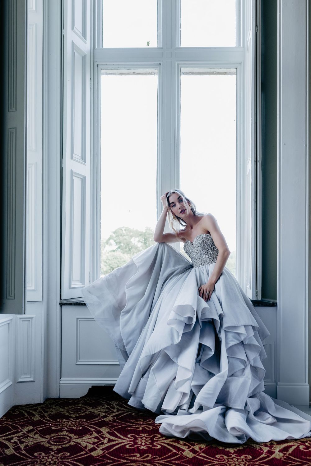 Ethereal bridal portrait featuring flowing silver-white gown against bright windows in a minimalist room.