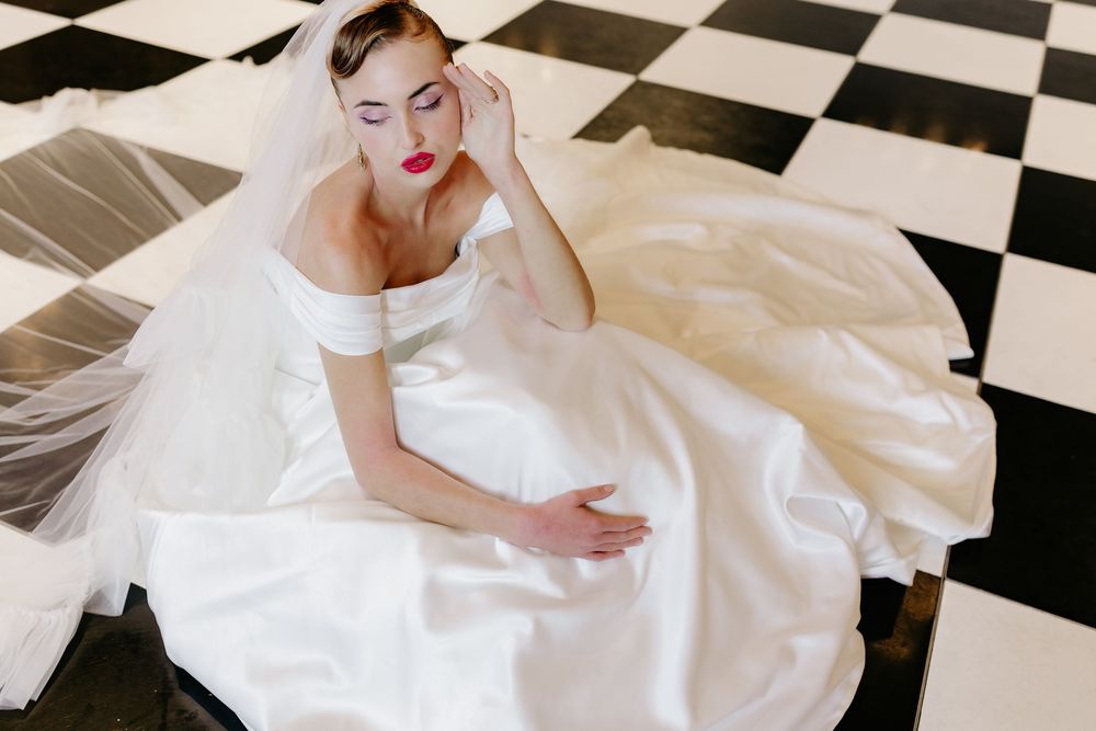 A person wearing a white wedding dress reclines on a black and white checkered floor.