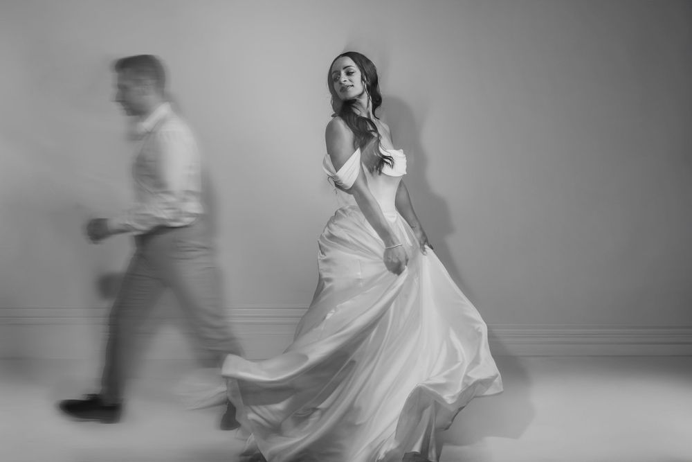 Black and white artistic wedding photo showing dancers in motion with flowing white dress and dramatic movement.