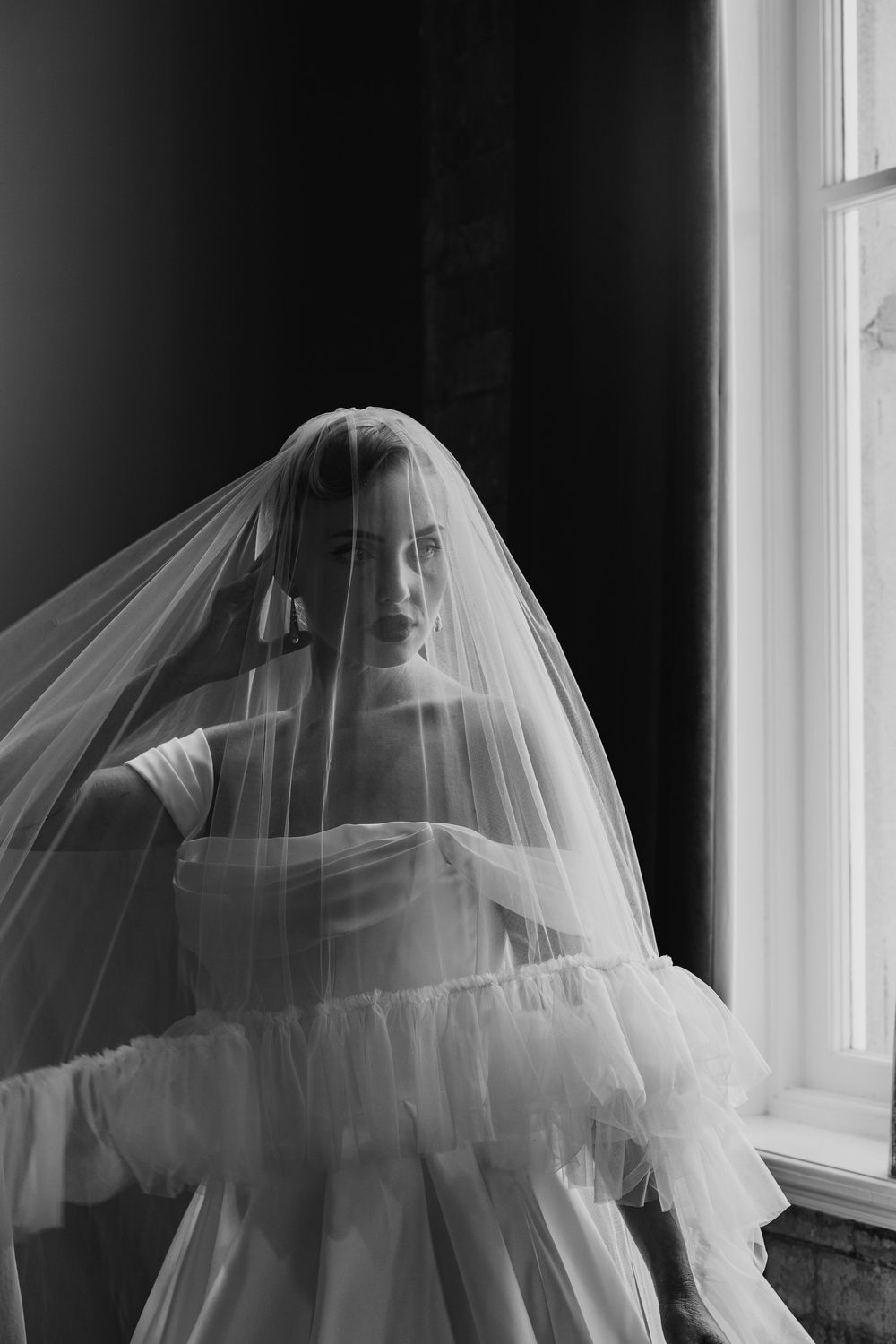 A haunting black and white photograph shows a wedding veil billowing across three window frames, casting ethereal shadows.
