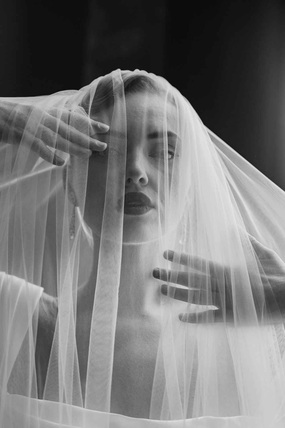 A series of hands manipulating and stretching delicate white tulle fabric against a dark background, creating flowing patterns.