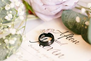 Black wedding band and diamond ring artistically photographed with pink roses and calligraphy.