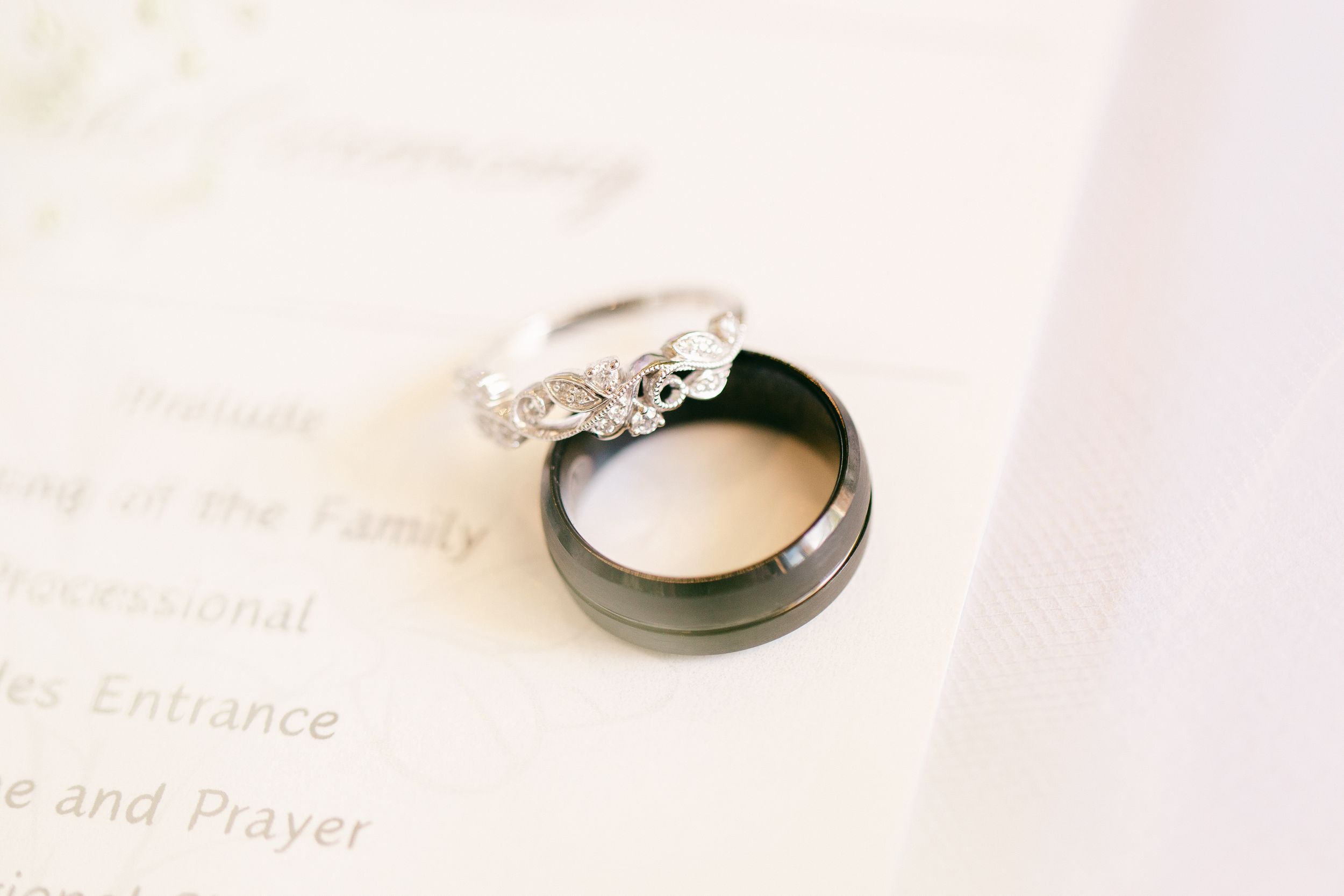 Wedding rings resting on white paper with elegant diamond and black band details.