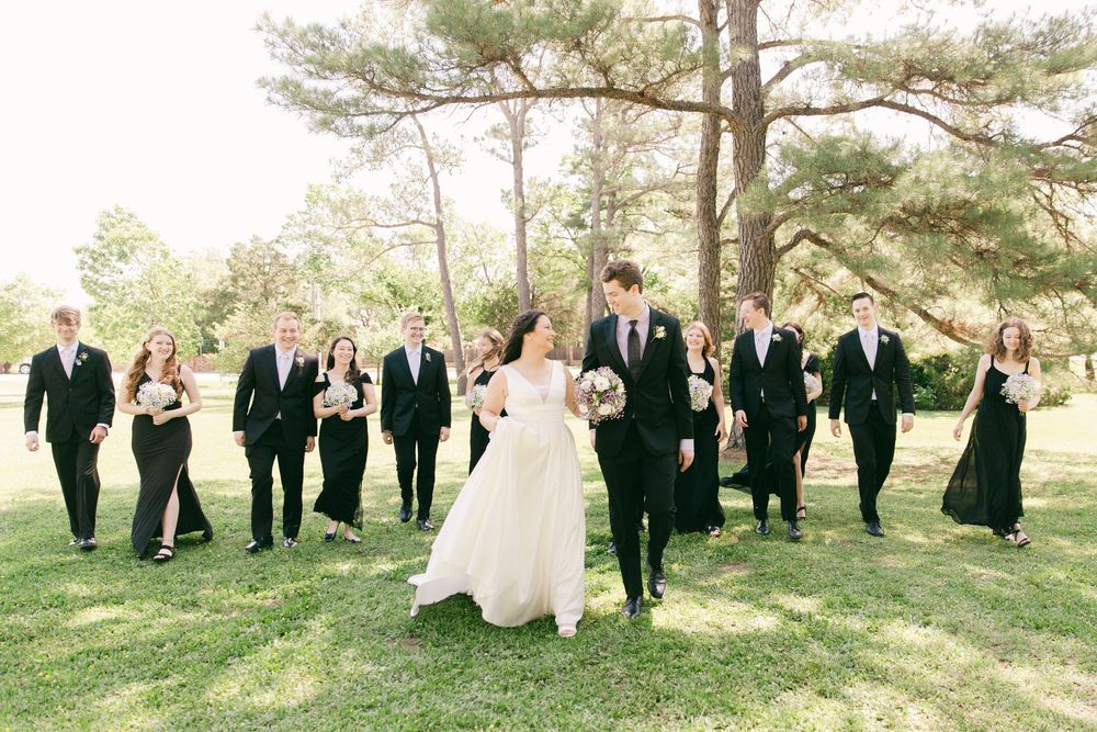 Wedding party poses together on grassy lawn with tall pine trees in background.