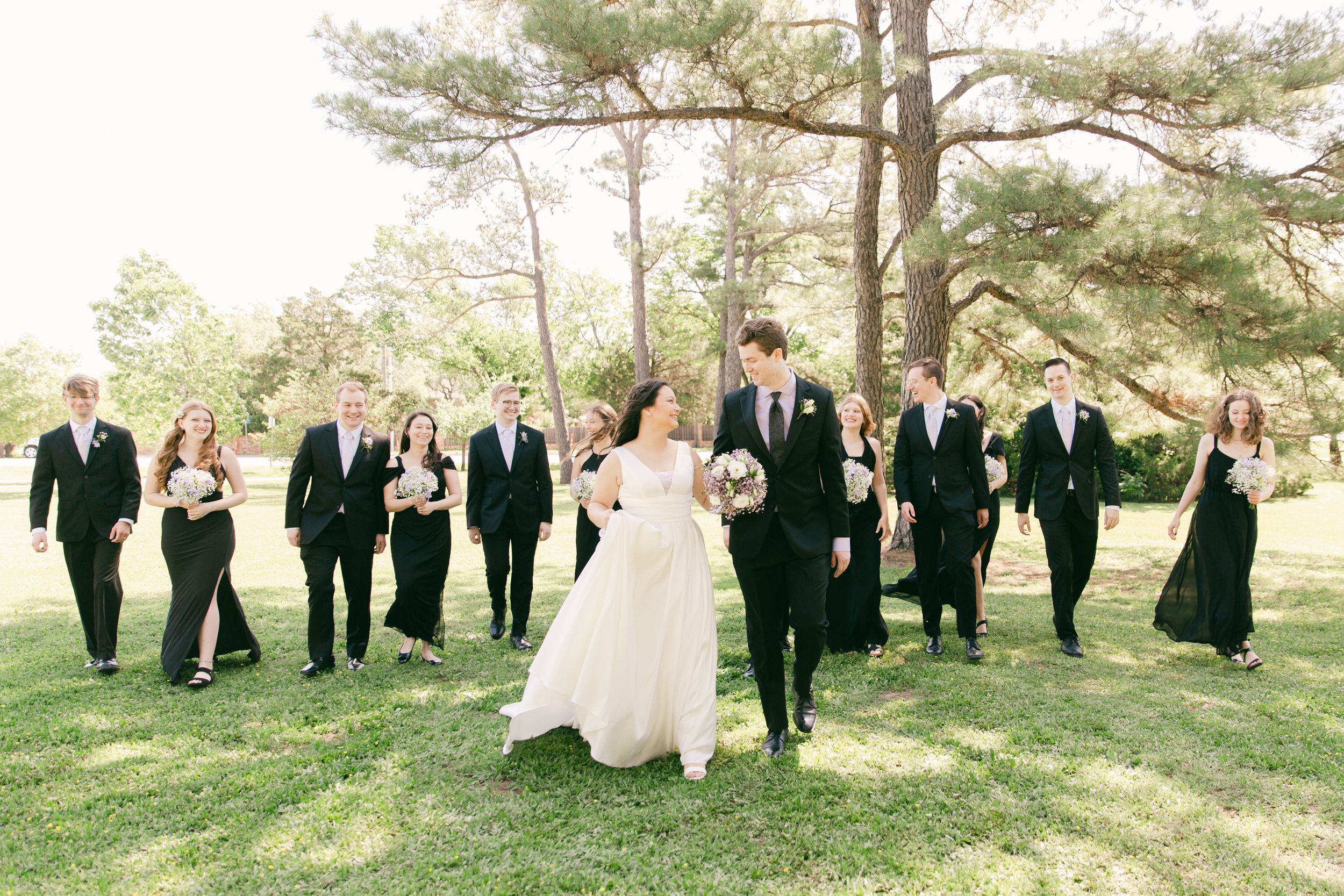 Wedding party poses together on grassy lawn with tall pine trees in background.