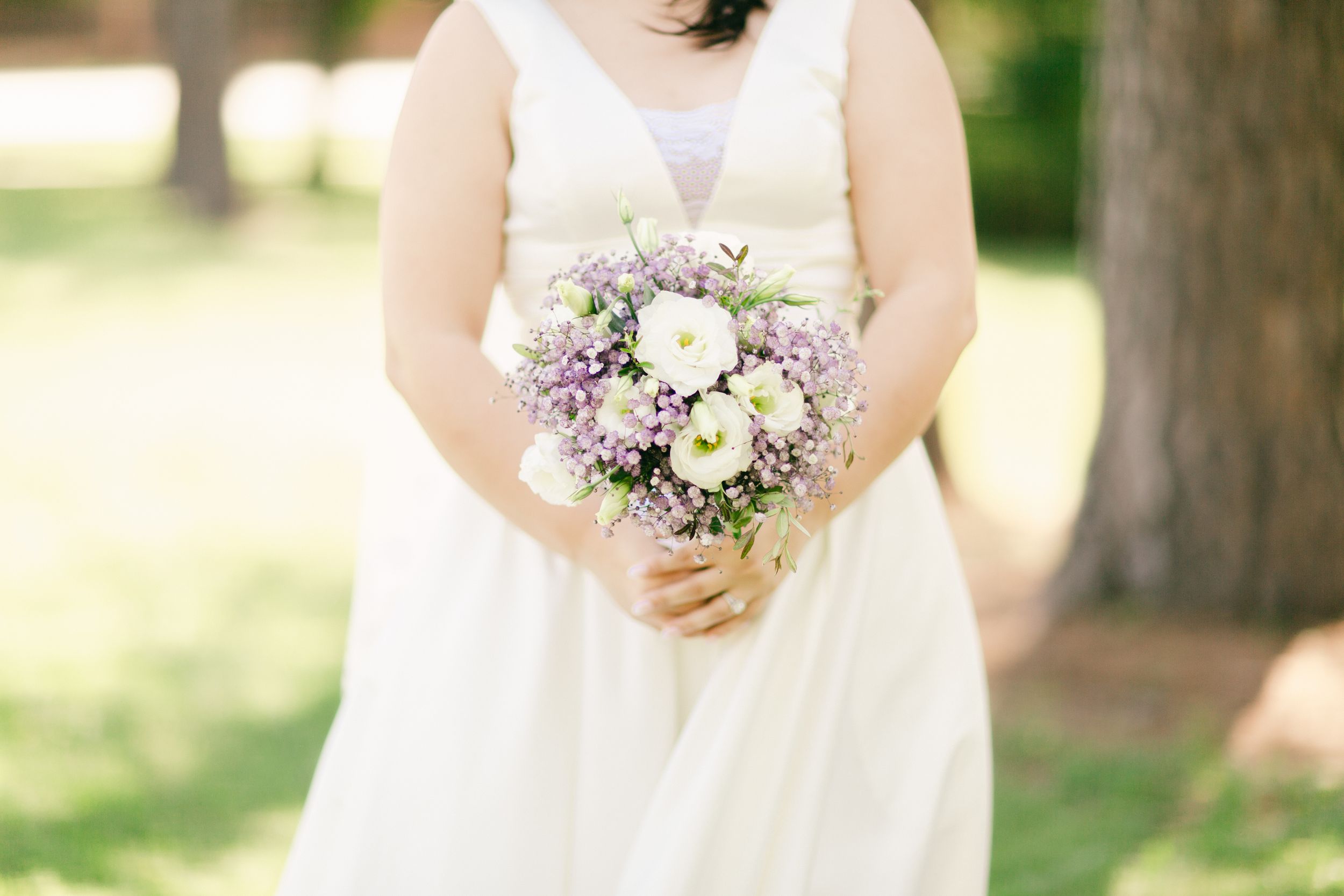 Close-up of a romantic purple and white wedding bouquet held against a white wedding dress.