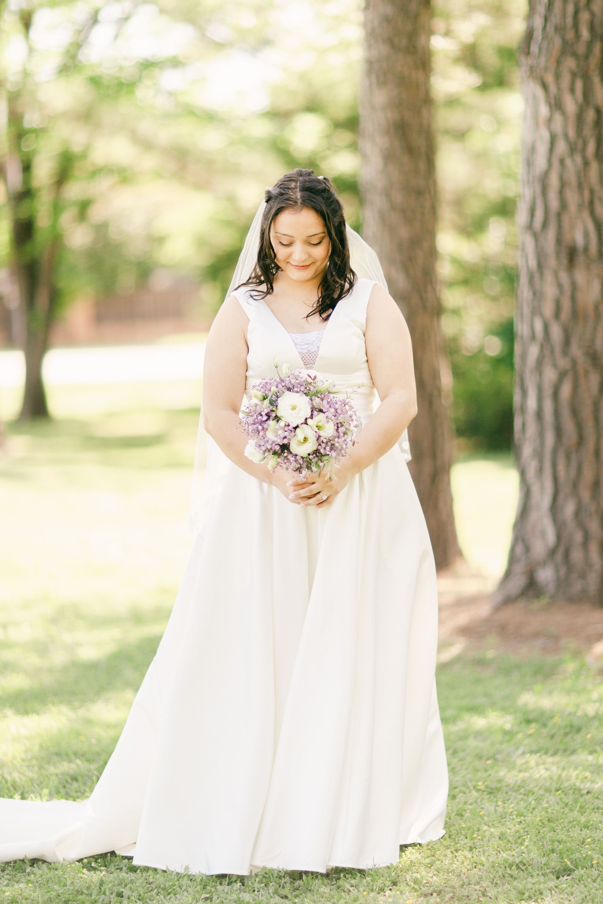 Elegant outdoor bridal portrait on grass beneath towering pine trees.