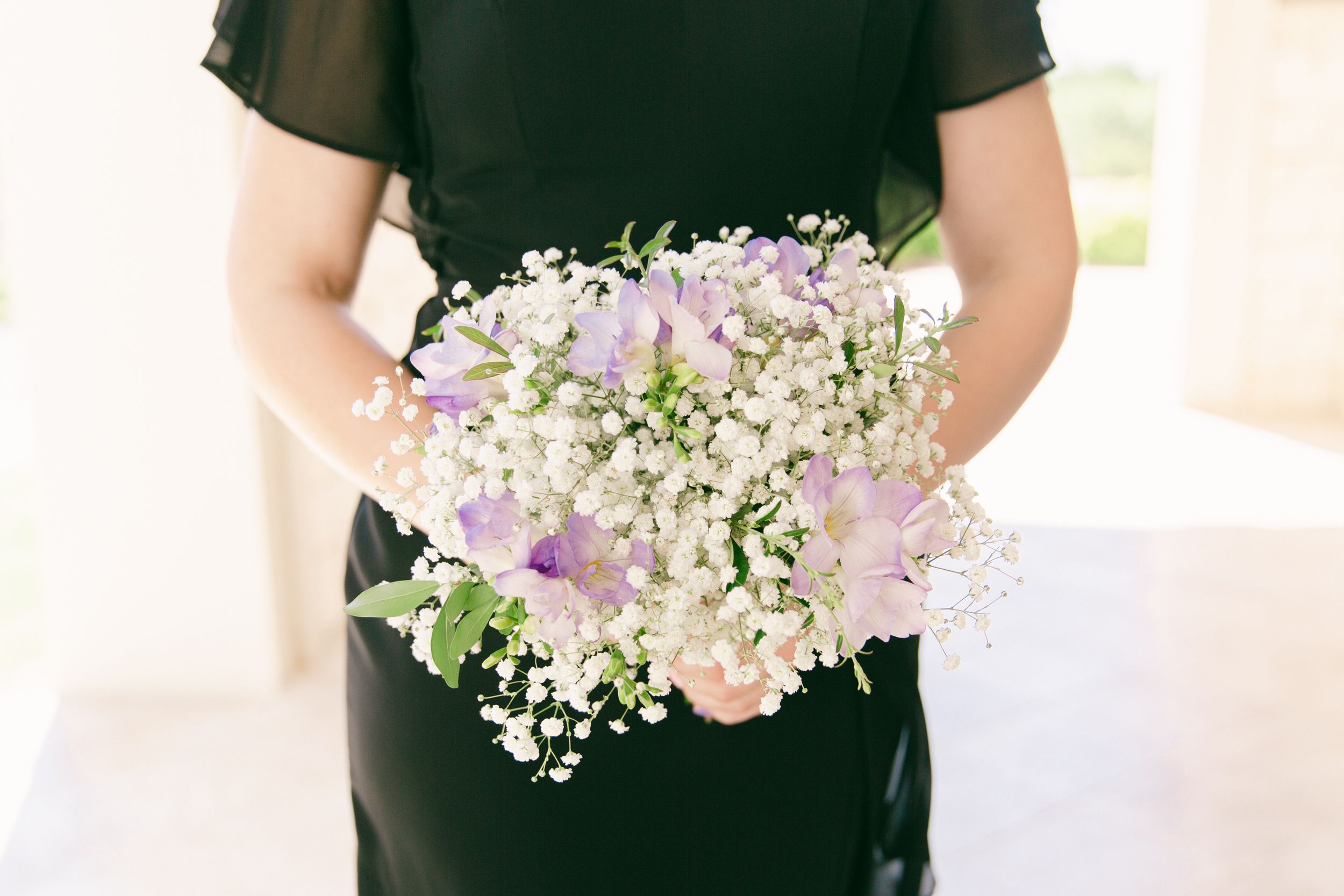 Delicate bouquet of purple and white flowers held in front of a black dress.