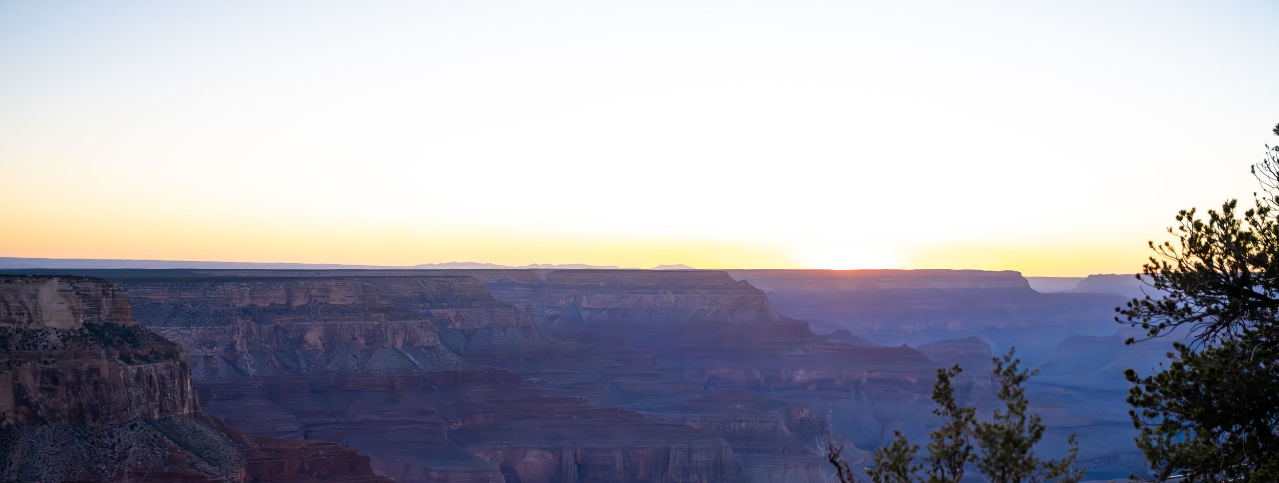 A serene sunset panorama captures the layered cliffs and vast expanse of a desert canyon landscape.