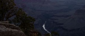 Winding Colorado River snakes through the deep Grand Canyon under a dark moody sky.
