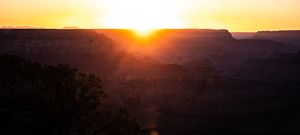 Stunning sunset silhouettes the Grand Canyon's majestic rock formations against an orange sky.