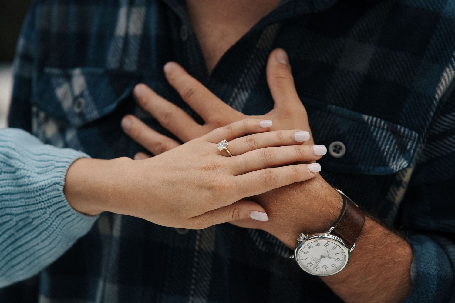 Close up of hands touching with one person wearing a silver wristwatch and blue sweater sleeve.