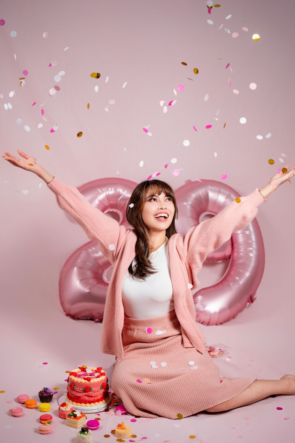 oyful girl throwing confetti in the air during her 20th birthday studio photoshoot on a pink backdrop in Auckland.