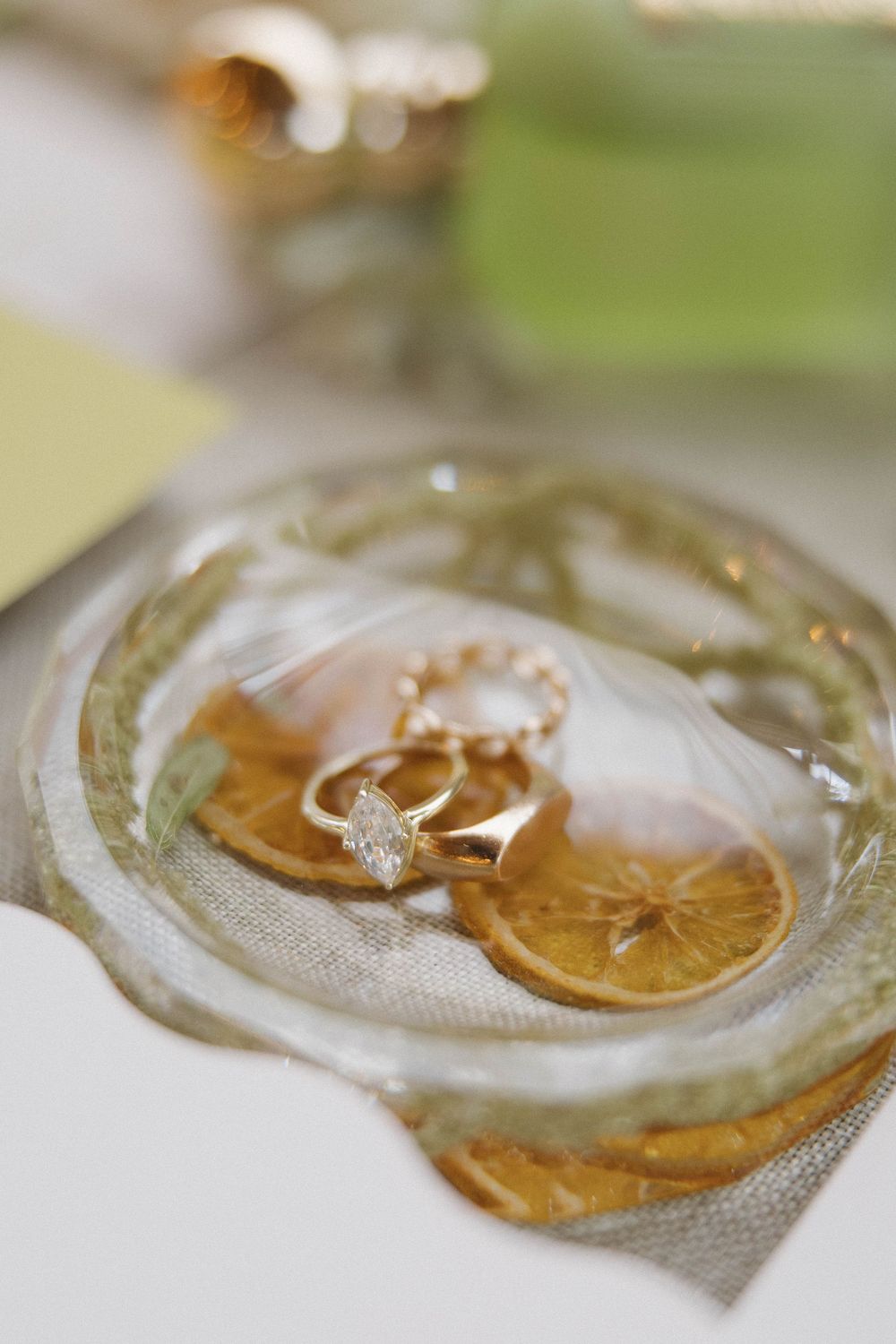 Diamond engagement ring placed on sliced citrus fruit in a delicate glass dish for a creative wedding detail photo.